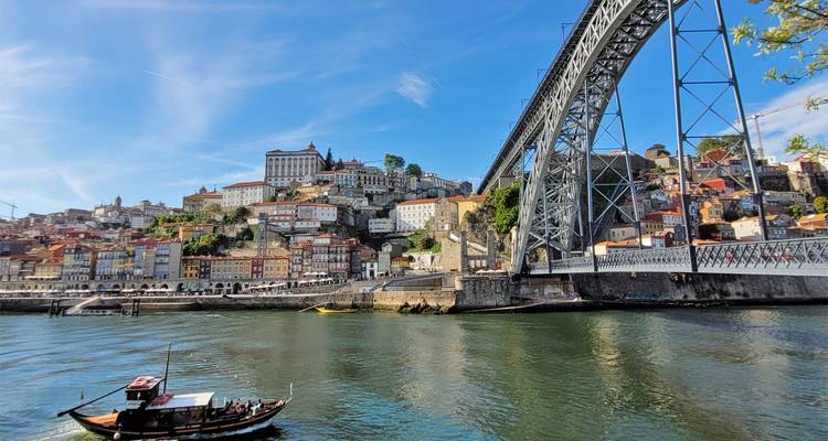 Dom Luís I Bridge spanning the Douro River with traditional rabelo boat passing below.