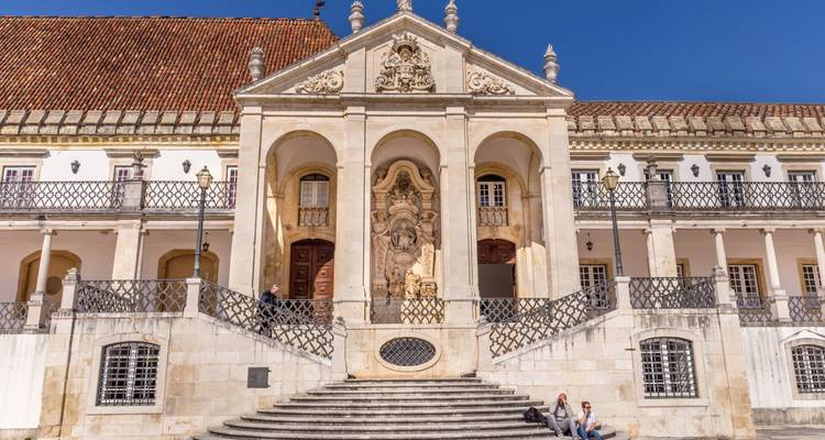 Historic university building with baroque portal, twin staircases and blue sky.