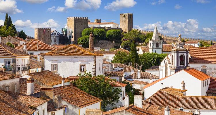 Medieval walls and castle towering above whitewashed houses in Óbidos, Portugal.