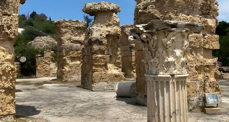 Vue rapprochée d'un chapiteau de colonne romaine sculpté au milieu de murs de grès altérés dans les ruines de Carthage.