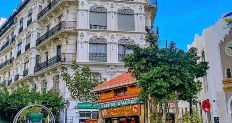Élégant bâtiment de l'époque coloniale avec balcons en fer forgé et boutiques au niveau de la rue sous un ciel bleu éclatant.