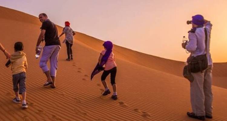 Familie wandert bei Sonnenuntergang eine Sanddüne hinauf und hinterlässt Fußspuren im warmen orangefarbenen Licht.