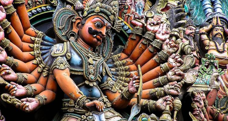 Ingewikkelde meervoudige armengod sculptuur met levendige kleuren en gedetailleerde ornamenten op een Zuid-Indiase tempel.