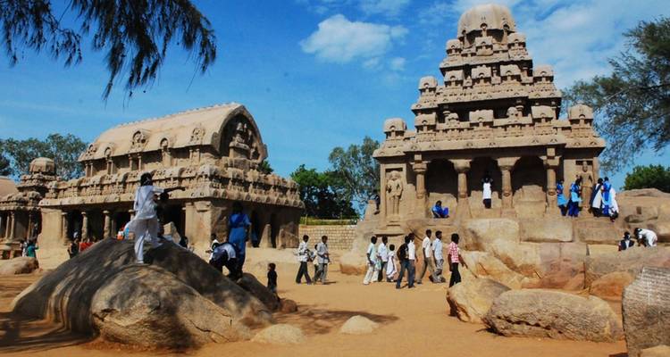 Bezoekers die oude uit rots gehouwen tempels en rotsblokken in Mahabalipuram verkennen onder een heldere blauwe hemel.