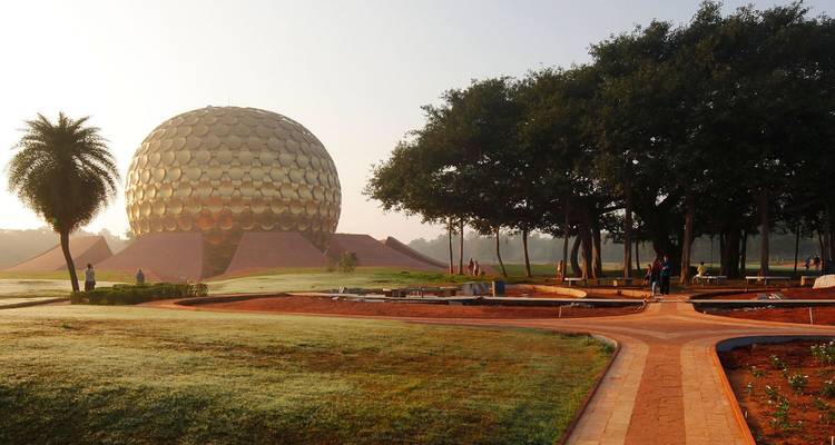 Gouden bolvormige Matrimandir-structuur die oprijst uit verzorgde gazons en rood-zandpaden in het vroege ochtendlicht.