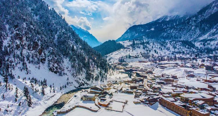 Village de montagne enneigé s'étendant le long d'une gorge fluviale sous des pics spectaculaires et un ciel lumineux.