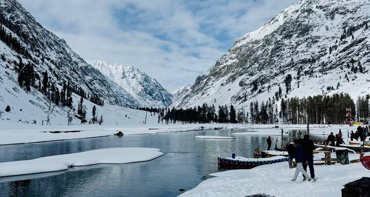 Lac alpin gelé bordé de pins chargés de neige et de pics spectaculaires avec des visiteurs emmitouflés sur la rive.