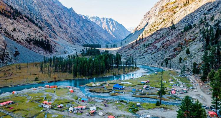 Panorama aérien d'un méandre de rivière turquoise, d'une île boisée et de tentes colorées installées au milieu de montagnes rocheuses escarpées.
