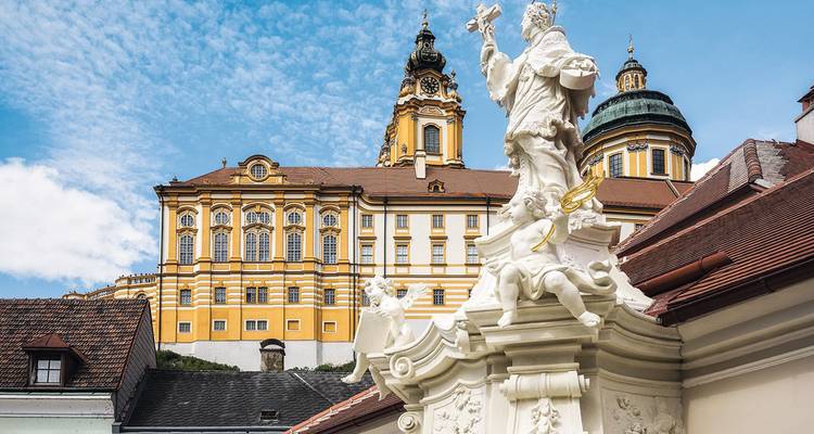 Primer plano de la ornamentada fachada barroca de la Abadía de Melk con una estatua blanca en primer plano bajo un cielo azul.