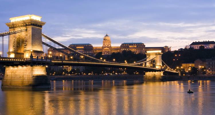 Vista nocturna del iluminado Puente de las Cadenas de Budapest atravesando el Danubio con el Castillo de Buda resplandeciendo al fondo.