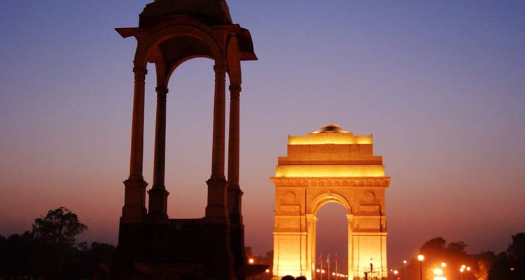 India Gate und Kuppelmonument dramatisch beleuchtet vor einem tiefen Dämmerungshimmel in Neu-Delhi.