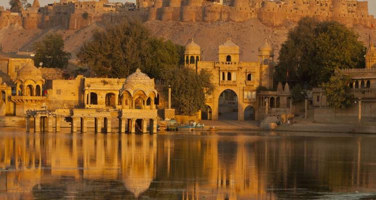 Goldene Tempel und Bögen des Gadsisar-Sees schimmern im Abendlicht vor der Kulisse einer Festung.