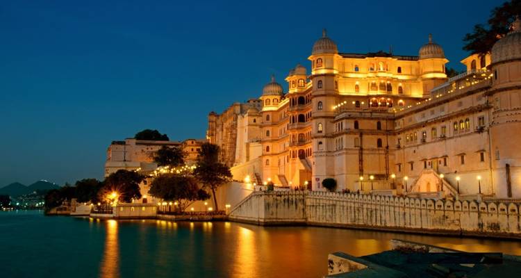 Beleuchteter Palastkomplex, der sich bei Dämmerung in einem ruhigen See spiegelt, mit tiefblauem Himmel.