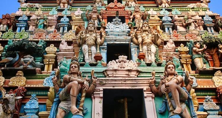 Farbenfroher, reich verzierter Gopuram-Turm, bedeckt mit hinduistischen Gottheiten, reicht in einen hellen Himmel.