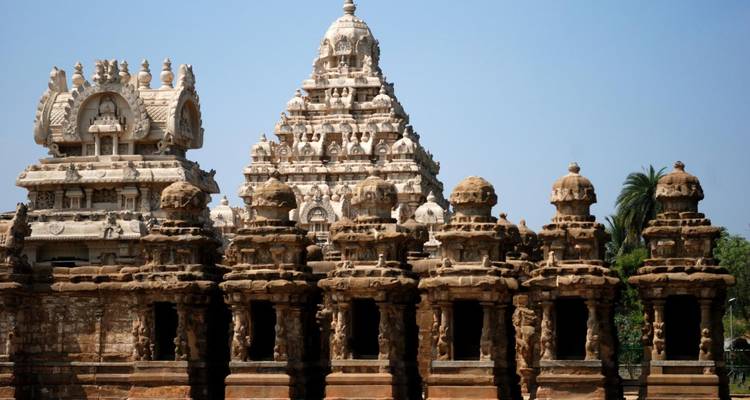 Sandfarbene Tempelstrukturen mit kunstvollen Schnitzereien und gestuften Türmen vor einem klaren Himmel.