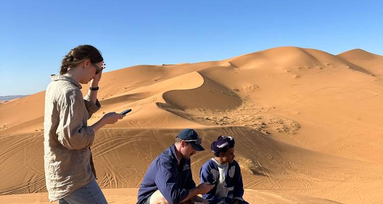 Reisende sitzen auf goldenen Sanddünen unter wolkenlosem blauem Himmel in der Sahara