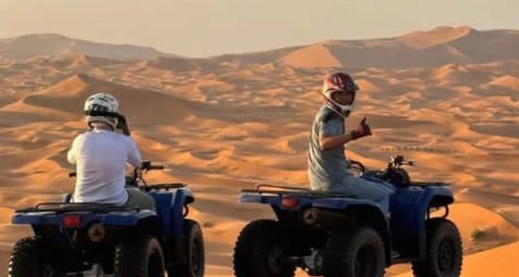 Zwei Fahrer auf blauen Quads blicken bei Sonnenuntergang auf ein weites welliges Sandmeer