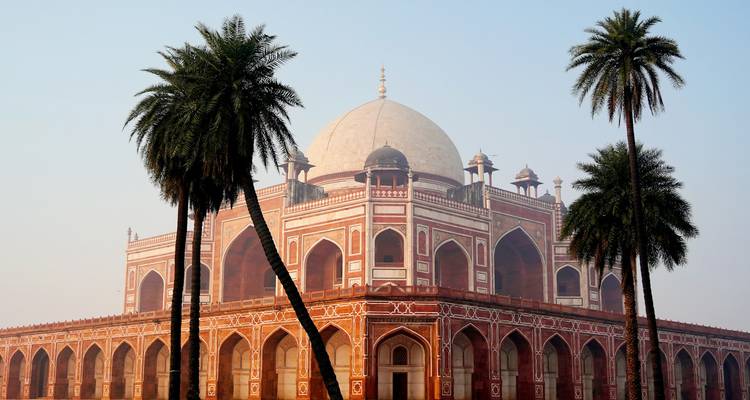 Le Tombeau d'Humayun avec ses grandes arches mogholes encadrées par de hauts palmiers contre un doux ciel matinal.