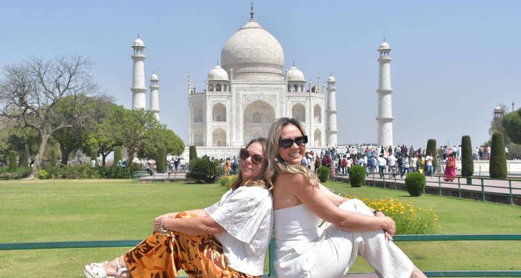 Deux femmes sont assises dos à dos sur un banc avec le Taj Mahal et les jardins derrière elles.