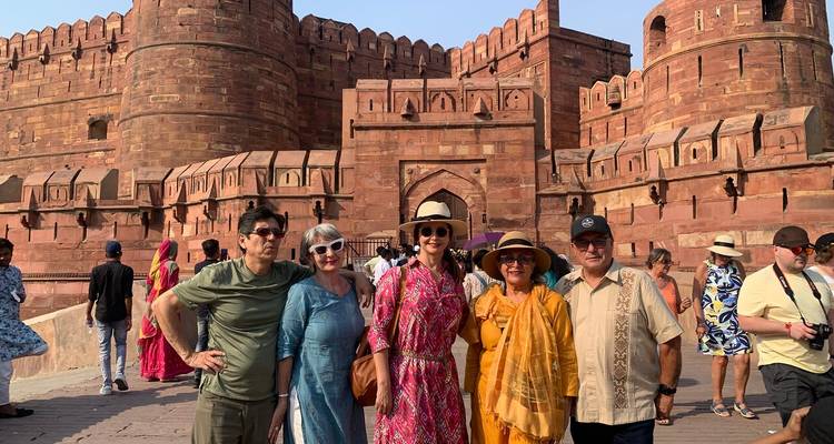Cinq touristes en vêtements colorés sourient devant les massifs murs de grès rouge du Fort d'Agra.