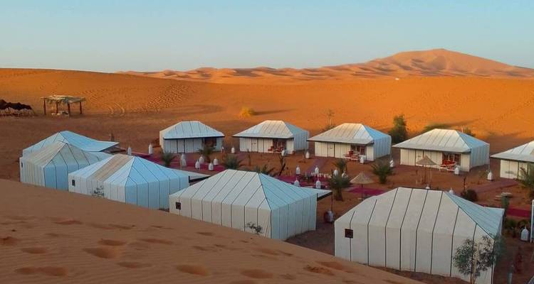Rijen witte luxe tenten staan tussen uitgestrekte oranje Sahara-duinen bij zonsopgang