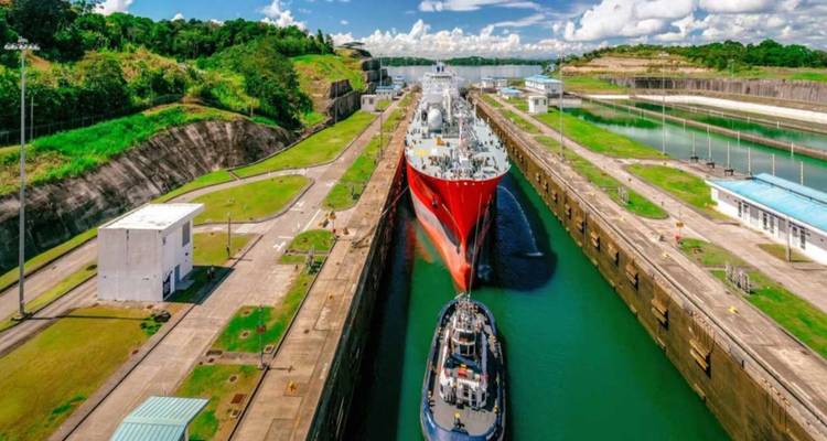 Gran barco de carga pasando por una esclusa del Canal de Panamá rodeado de exuberantes riberas verdes bajo un cielo brillante.