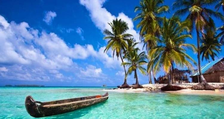 Escena de isla tropical con agua turquesa, canoa de madera tallada y palmeras altas bajo un cielo azul vívido.