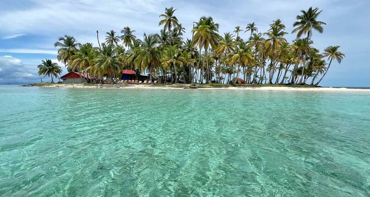 Pequeña isla tropical bordeada de palmeras inclinadas rodeada por un mar turquesa cristalino y poco profundo.