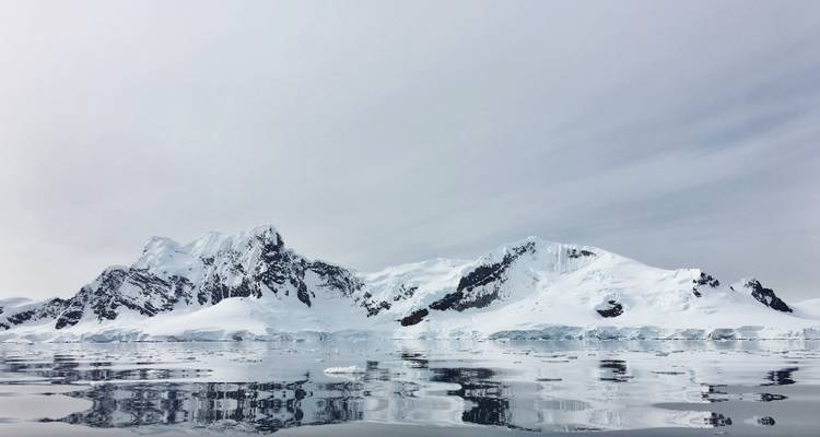 Majestueuze Antarctische bergketen bedekt met sneeuw weerspiegeld in stille ijzige wateren.