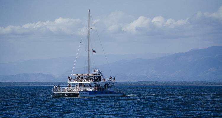 Catamaran vol passagiers zeilend op open blauwe zee tegen verre bergen.