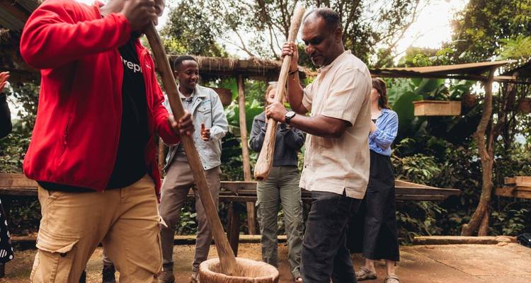 Les visiteurs et les habitants pilent ensemble le grain à l'aide de gros pilons en bois dans un cadre en plein air.