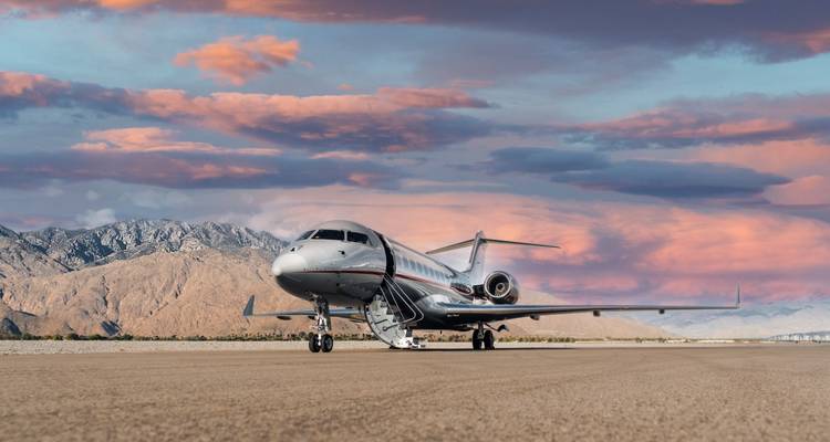 Eleganter Privatjet auf der Startbahn mit Wüstenbergen und leuchtend rosa Sonnenuntergangswolken im Hintergrund.