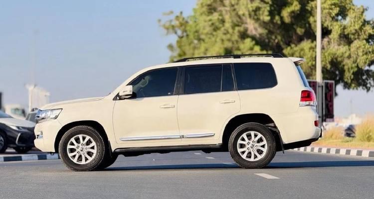 Seitenansicht eines beigen 4x4 SUV, der auf einer asphaltierten Straße geparkt ist, mit unscharfen Bäumen im Hintergrund.