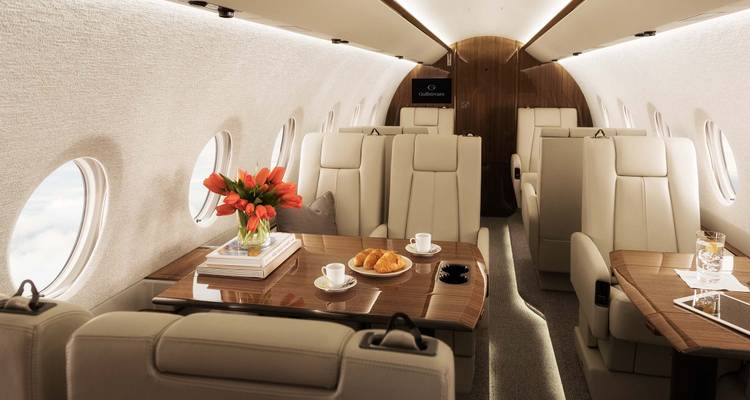 Helle Privatjet-Kabine mit cremefarbenen Sitzen, Holztischen, Blumen und angerichtetem Frühstücksgebäck.