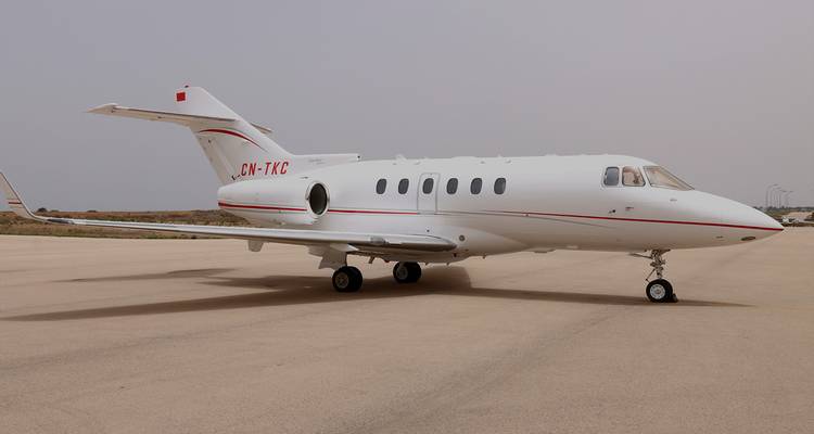 Klein wit privévliegtuig met Marokkaanse vlag geparkeerd alleen op lege landingsbaan onder bewolkte hemel.