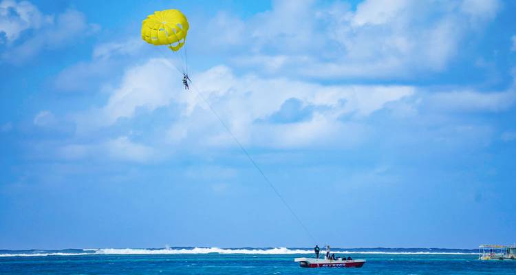 Paracaídas amarillo muy alto sobre el océano remolcando un barco con participantes haciendo parasailing