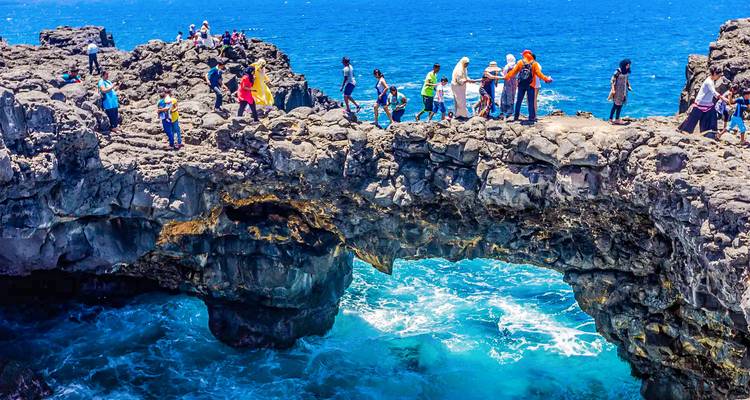 Visitantes caminando sobre un arco natural de basalto sobre olas turquesas estrellándose en Pont Naturel