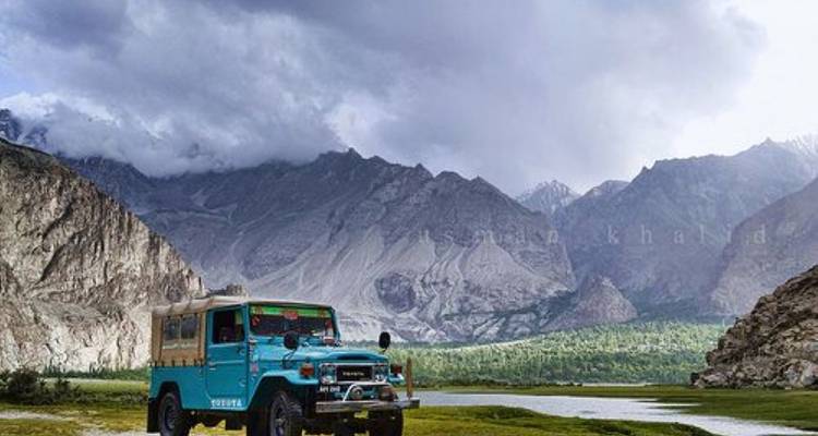 Jeep bleu vintage garé à côté d'une rivière glaciaire dans une vallée rocheuse spectaculaire.