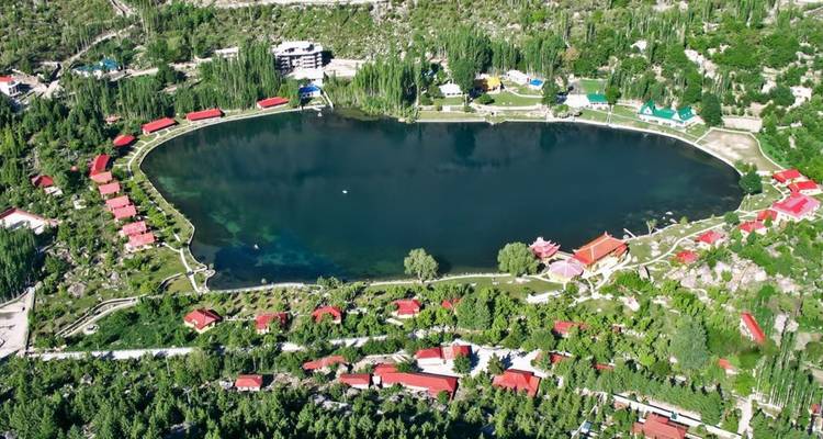 Vue aérienne d'un lac ovale encadré par des arbres verts et des chalets aux toits rouges.
