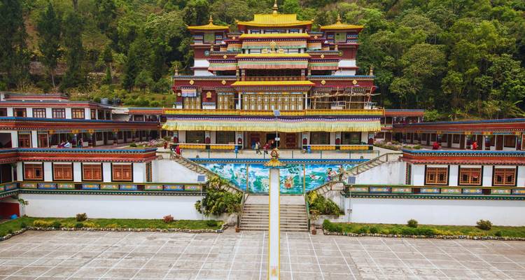 Farbenfrohe, mehrstöckige buddhistische Klosteranlage, umrahmt von üppig bewaldeten Hügeln, gesehen vom Hofeingang aus.
