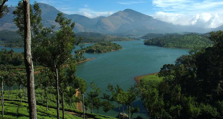 Réservoir serein serpentant entre des pentes montagneuses verdoyantes sous un ciel lumineux.