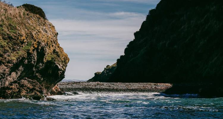 Smalle zeestraat begrensd door steile, beschaduwde kliffen en ruige water eronder.