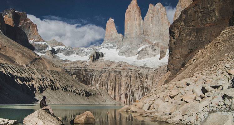 Un voyageur assis sur un rocher admire les tours de granit emblématiques qui s'élèvent au-dessus du lac glaciaire turquoise.