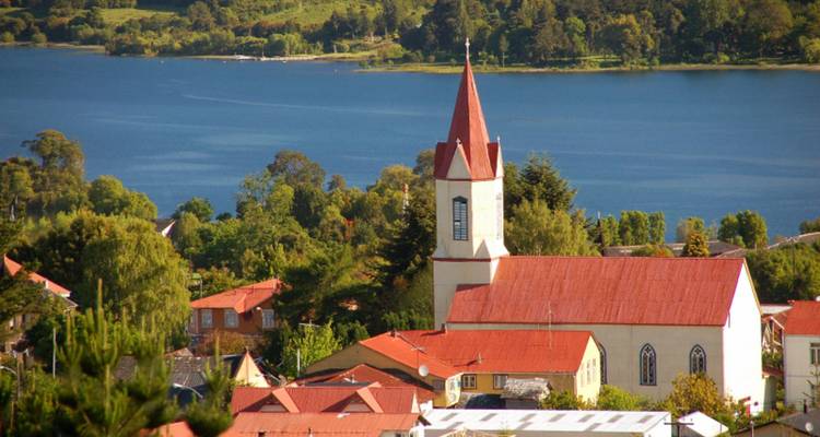 Rotdachige Kirche überblickt einen blauen See, der von grüner Landschaft umgeben ist.
