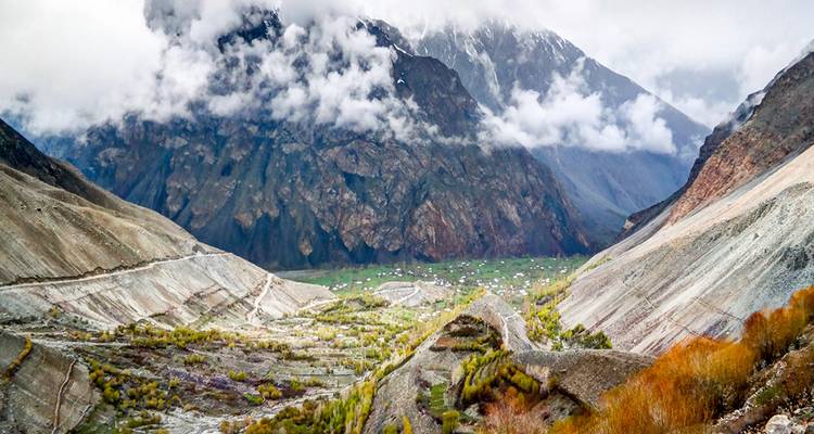 Misty mountain landscape with clouds hugging steep cliffs above a green valley floor.