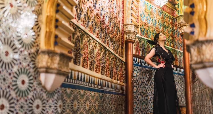 Mujer elegante posa con confianza dentro de un interior de palacio marroquí ornamentadamente embaldosado con mosaicos vibrantes.