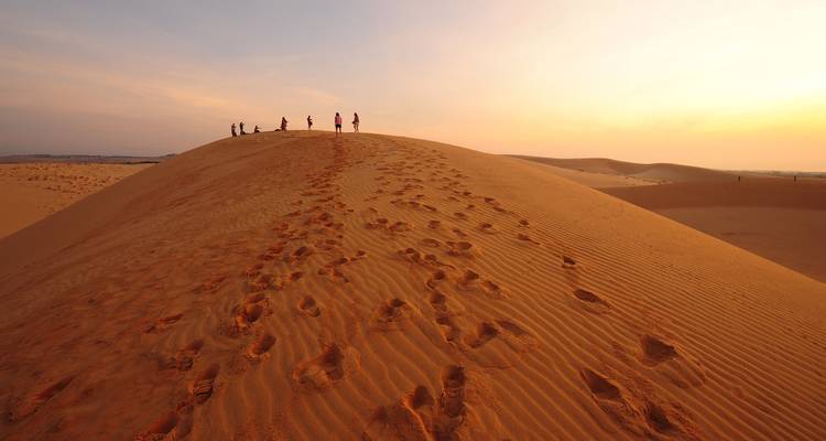 Personas caminando por la cresta de una duna de arena alta al atardecer dejando huellas en la arena