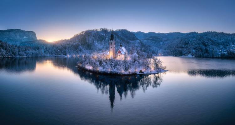 Serene winterdageraad over het Meer van Bled met zijn met sneeuw bestoven eilandkerkje weerspiegeld in stilstaand water.