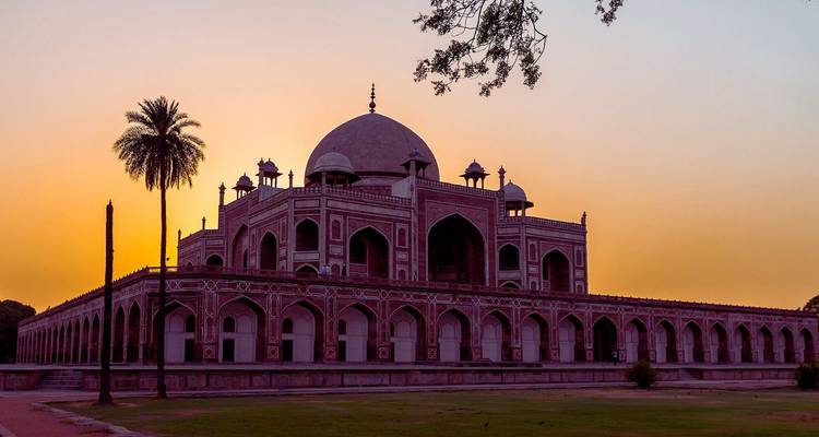De tombe van Humayun afgezet tegen een warme zonsonderganghemel met palmboom als omlijsting.