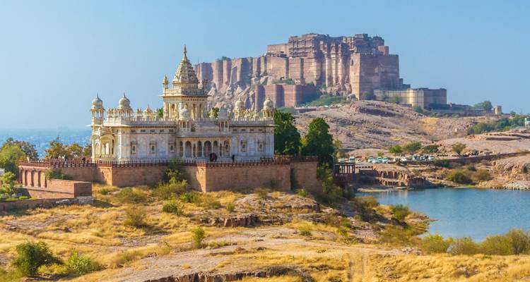 Wit marmeren Jaswant Thada naast blauw meer met imposante Mehrangarh Fort op rotsachtige bergkam erachter.